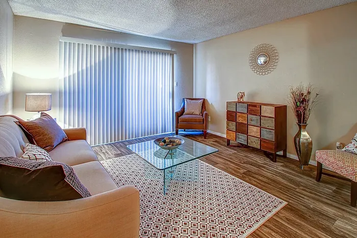 Cozy living room featuring a beige sofa, stylish glass coffee table, and natural light streaming through vertical blinds.