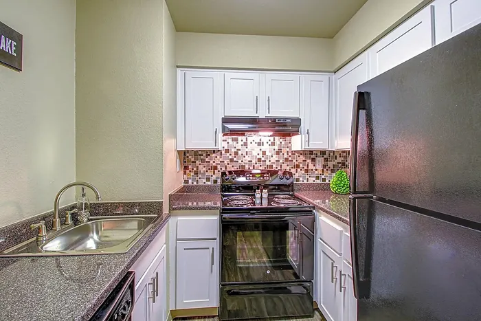 Contemporary kitchen with sleek black appliances, granite countertops, and mosaic tile backsplash.