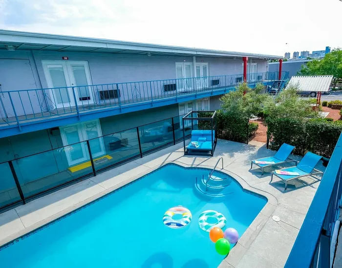 Vibrant outdoor pool surrounded by modern two-story apartment complex with lounge chairs and colorful pool floats.