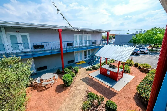 Colorful two-story apartment building with vibrant outdoor courtyard, featuring string lights and lush greenery.