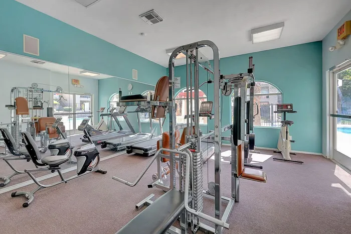 Bright and modern fitness center with state-of-the-art equipment, showcasing treadmills, weight machines, and an inviting pool view.