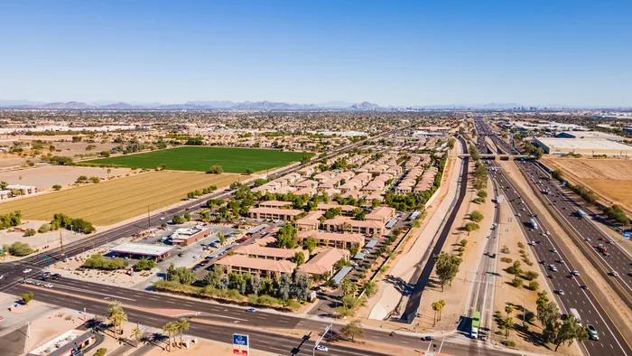 Captivating aerial view of a sprawling residential community with lush landscapes beside a bustling highway, showcasing proximity to amenities and expansive green fields.