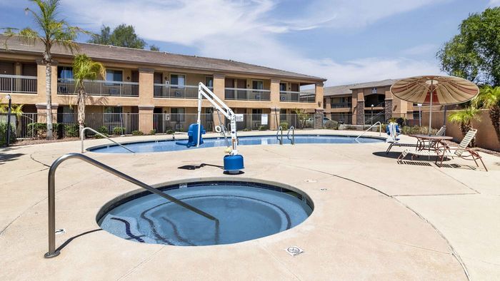 Charming apartment complex featuring a sunlit pool area with a relaxing hot tub, surrounded by lush palm trees and stylish lounge chairs for a perfect outdoor escape.