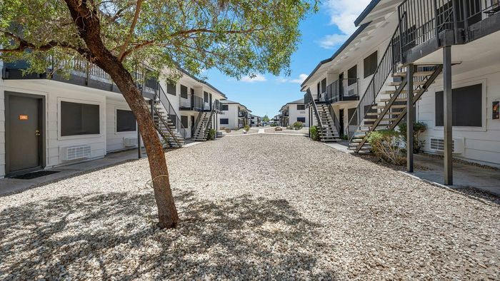 Charming courtyard view of modern apartment complex with white facades, balconies, and lush greenery under a sunny sky.