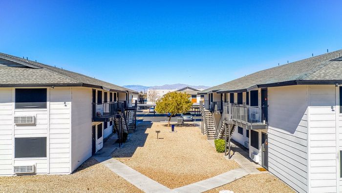 Charming apartment complex with modern architecture, spacious courtyards, and mountain views under a clear blue sky.