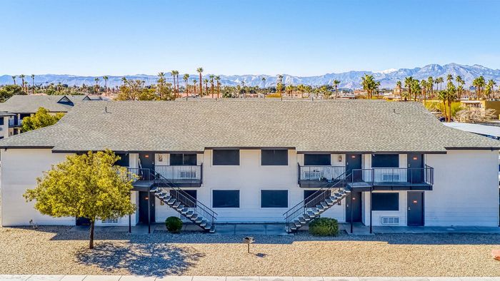 Charming two-story apartment building with balconies, nestled in a scenic setting with mountain views and palm trees.