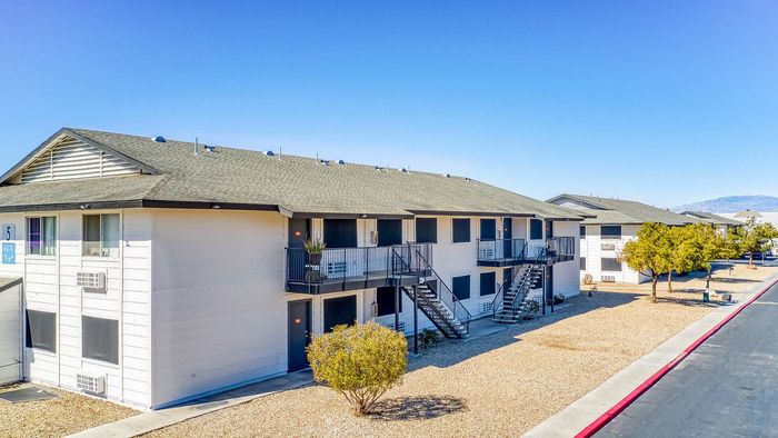 Charming two-story apartment complex with modern design, surrounded by a serene landscape and clear blue sky.