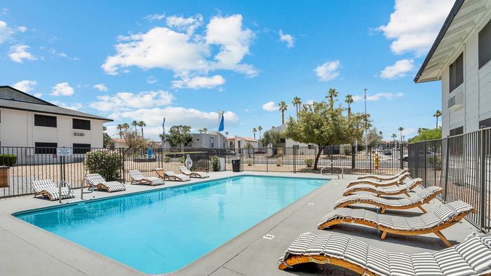 Inviting outdoor pool area with stylish lounge chairs under a sunny blue sky, perfect for relaxation and leisure.