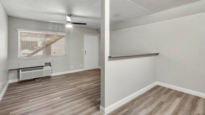 Modern apartment showcasing sleek wood flooring, ample natural light from large windows, and a stylish ceiling fan.