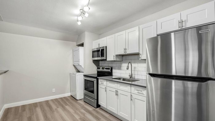 Modern kitchen with sleek stainless steel appliances, elegant white cabinetry, and stylish wood flooring, featuring a convenient in-unit washer and dryer.