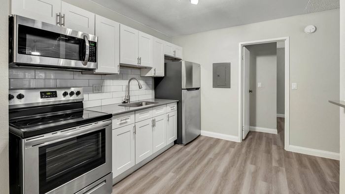 Modern kitchen with sleek stainless steel appliances, elegant white cabinetry, and chic wood-style flooring.