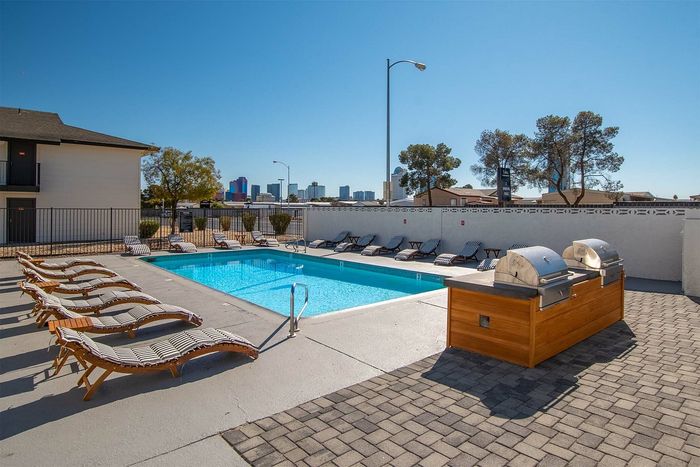 Inviting outdoor pool area with sun loungers and a modern BBQ station, perfect for relaxation and entertaining while enjoying a cityscape view.