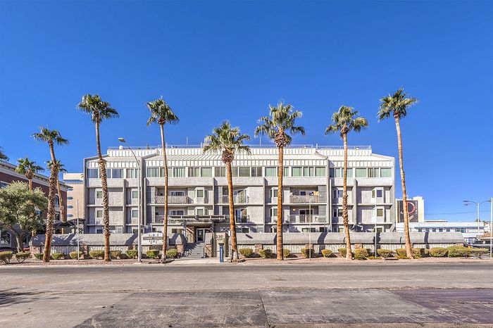 Modern apartment complex with sleek architecture, framed by tall palm trees under a bright blue sky.