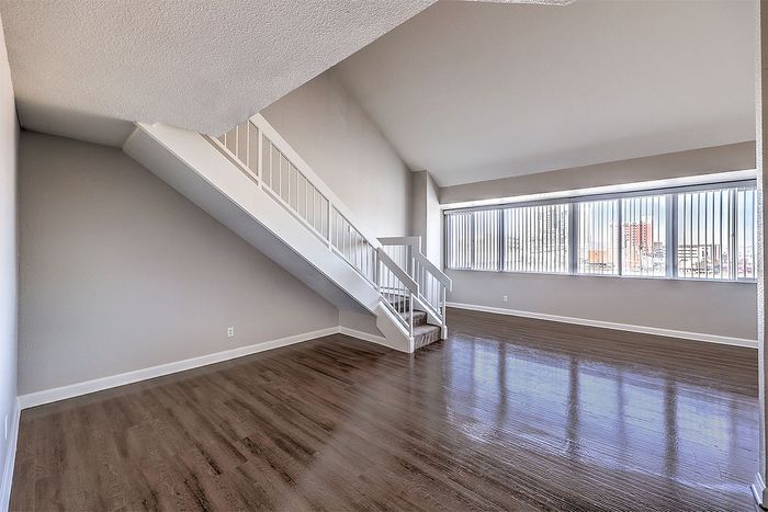 Bright and airy loft apartment with sleek hardwood floors, large windows offering city views, and a stylish staircase.