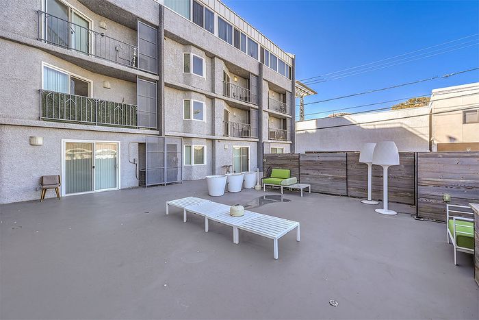 Spacious outdoor patio area with modern apartment balconies, sleek seating, and vibrant decor against a clear blue sky.