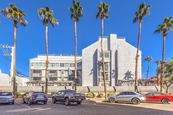 Modern apartment building with sleek architecture surrounded by tall palm trees under a clear blue sky.