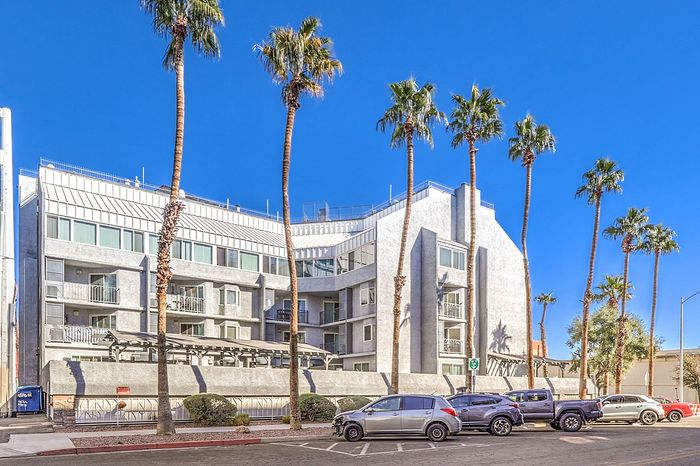 Modern apartment building with sleek architecture surrounded by tall palm trees against a clear blue sky.