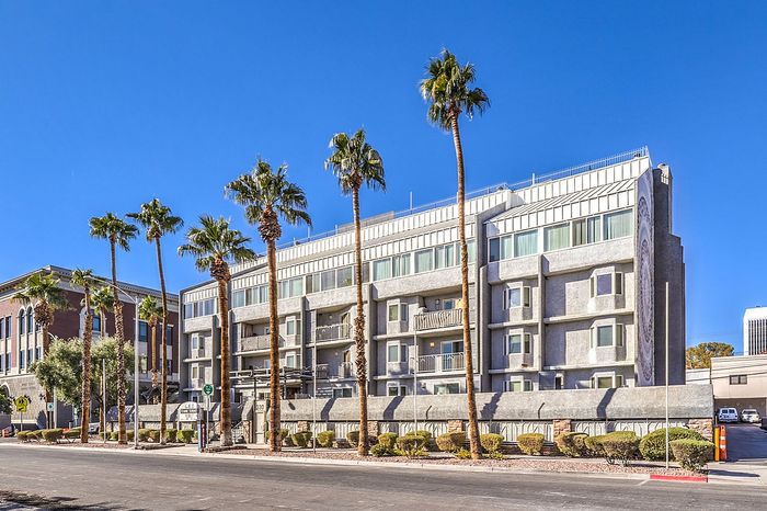 Modern apartment building with sleek design, framed by tall palm trees under a clear blue sky.