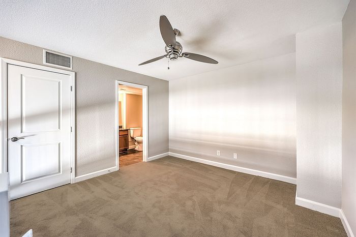 Bright bedroom featuring plush carpet, a sleek ceiling fan, and doorway access to a modern en-suite bathroom.