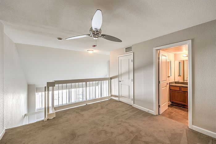 Bright loft space with modern ceiling fan, cozy carpeting, and adjacent bathroom for ultimate convenience.