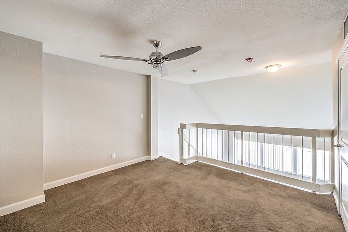 Bright upper-level loft space with plush carpeting and modern ceiling fan, offering a cozy and versatile area. The open railing design provides an airy view overlooking the room below.