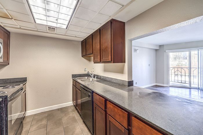 Bright and modern kitchen with sleek countertops and ample cabinetry, leading to a sunlit living area with sliding glass doors.