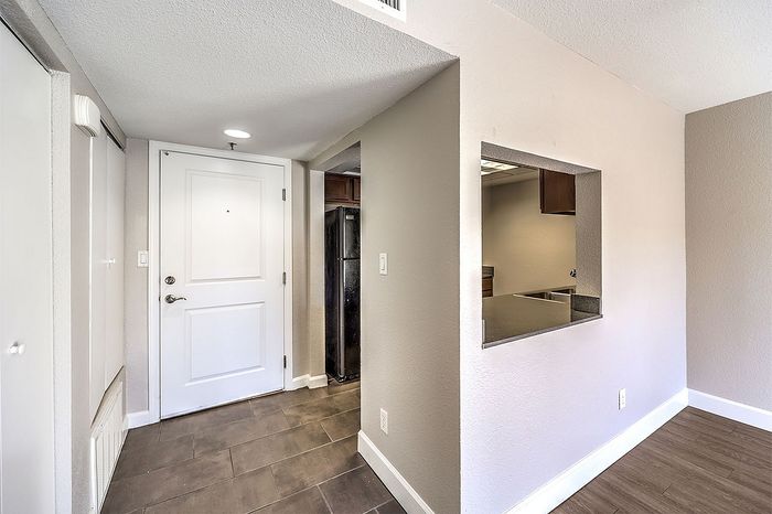 Inviting apartment entryway with sleek tile flooring, modern white door, and a peek into the contemporary kitchen.