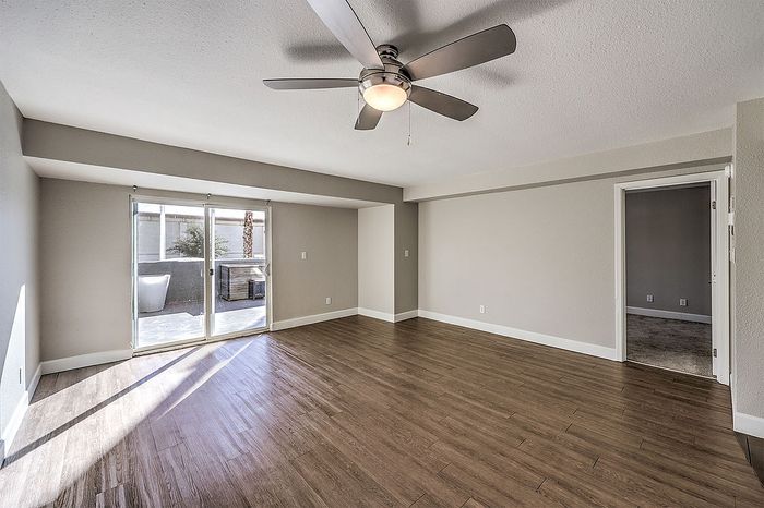 Bright and airy living room with elegant wood flooring, modern ceiling fan, and sliding glass doors leading to a serene outdoor patio.