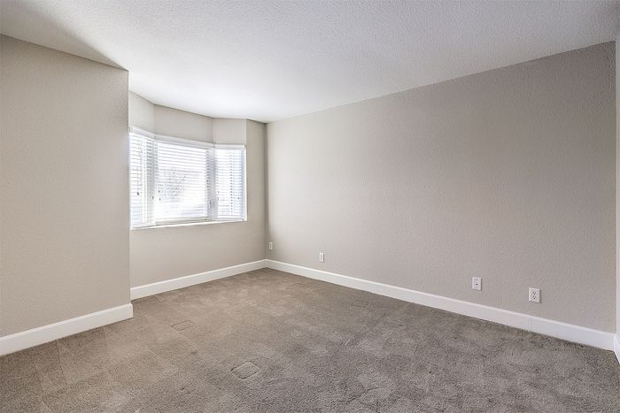 Bright and spacious room with modern neutral tones, large bay window, and plush carpet flooring.
