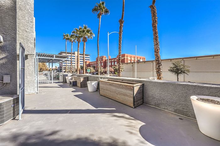Chic urban patio with palm trees, spacious seating, and city views under a bright blue sky.