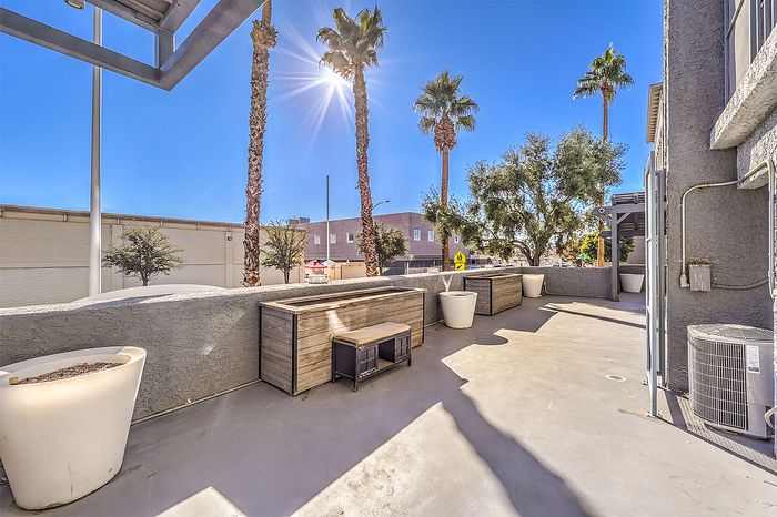 Sunlit outdoor patio featuring elegant planters, modern seating, and towering palm trees creating a serene oasis.