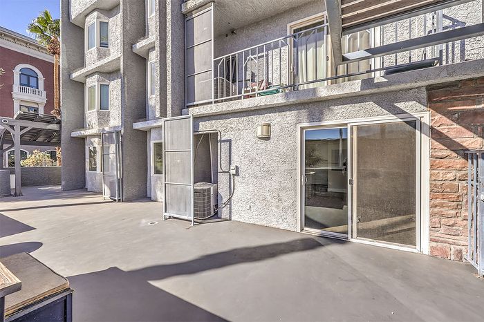 Modern apartment exterior with private balcony, expansive patio, and elegant architectural features under a clear blue sky.