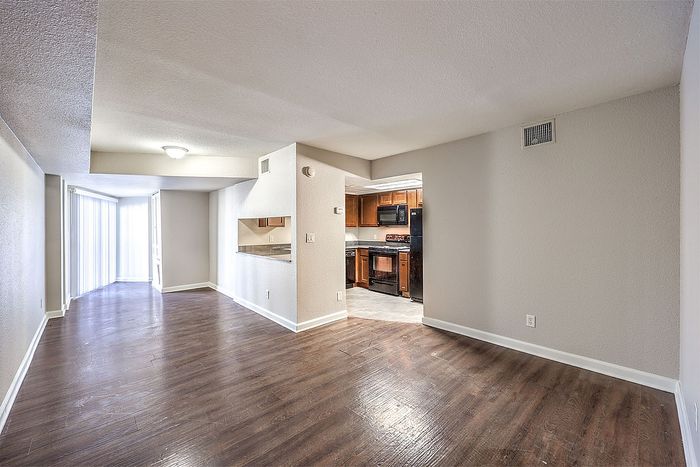 Bright and inviting open-floor apartment with elegant hardwood flooring, showcasing a spacious living area and a stylish, modern kitchen.