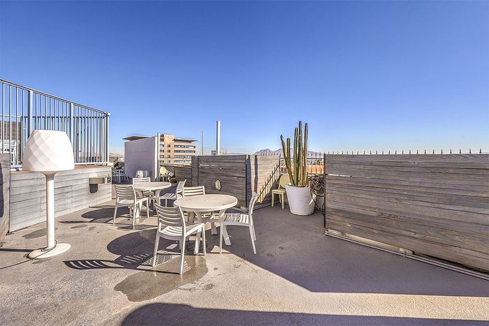 Chic rooftop terrace featuring modern patio furniture, potted cactus, and stunning city view under clear blue skies.