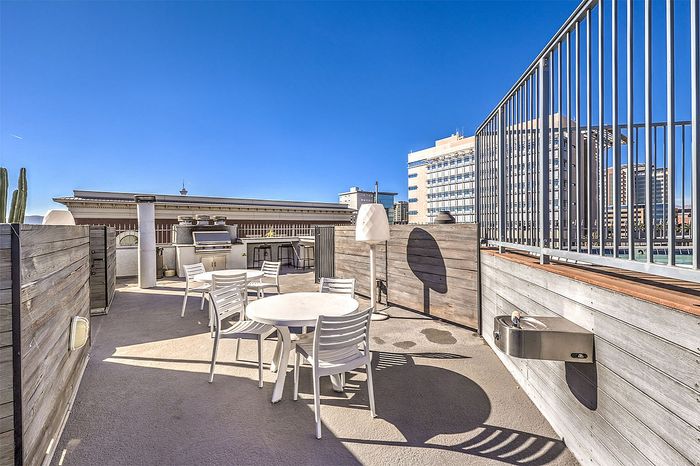 Stunning rooftop patio featuring sleek white furniture, a modern barbecue grill, and vibrant city views under a clear blue sky.