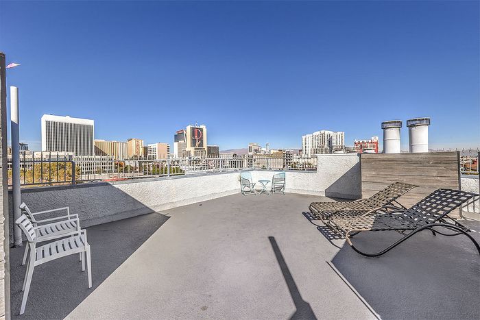 Expansive rooftop terrace offering breathtaking city skyline views with cozy seating and sun loungers under a clear blue sky.
