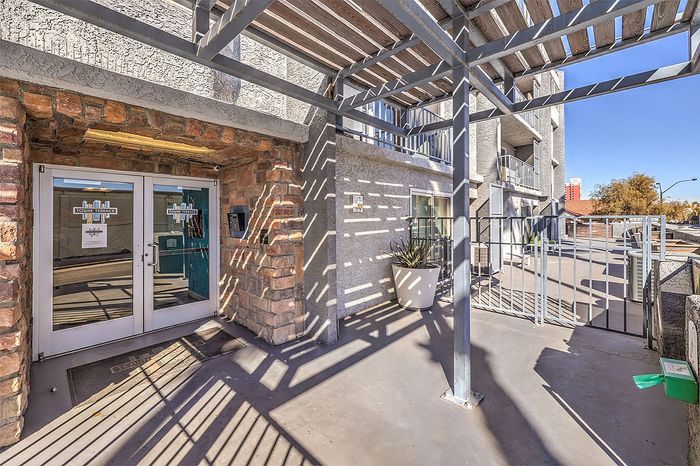 Inviting apartment entrance with modern pergola design, rustic brick accents, and clear glass doors leading into the cozy lobby.
