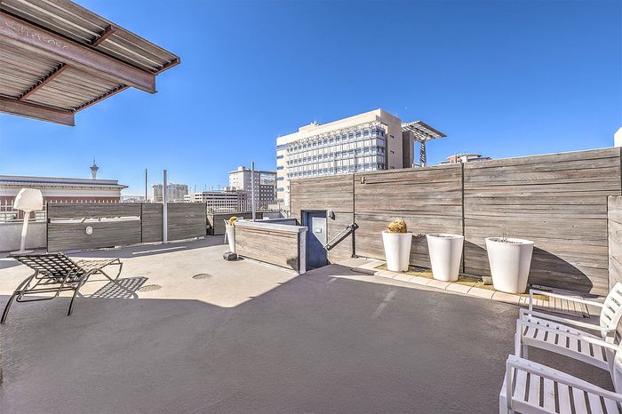 Chic urban rooftop patio with modern lounge chairs, offering stunning city views and ample sunlight.