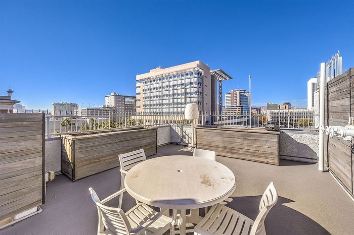 Sunny rooftop terrace with a round dining table, city skyline views, and modern fencing.