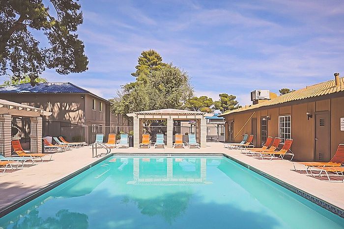 Inviting apartment complex pool area with bright lounge chairs and a pergola, perfect for relaxing under the sunny skies.