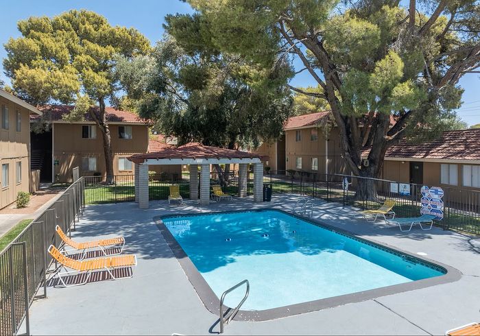 Charming apartment complex featuring a sparkling pool, surrounded by lush greenery and inviting lounge chairs for relaxation.