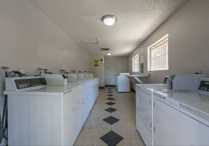 Bright and spacious laundry room featuring modern washers and dryers with ample lighting and a neat tiled floor.