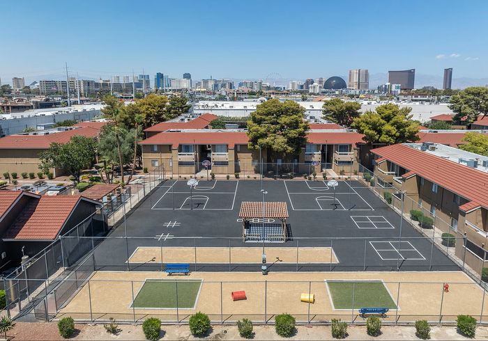 Charming apartment complex with red-tiled rooftops, featuring a modern sports court and vibrant skyline backdrop.