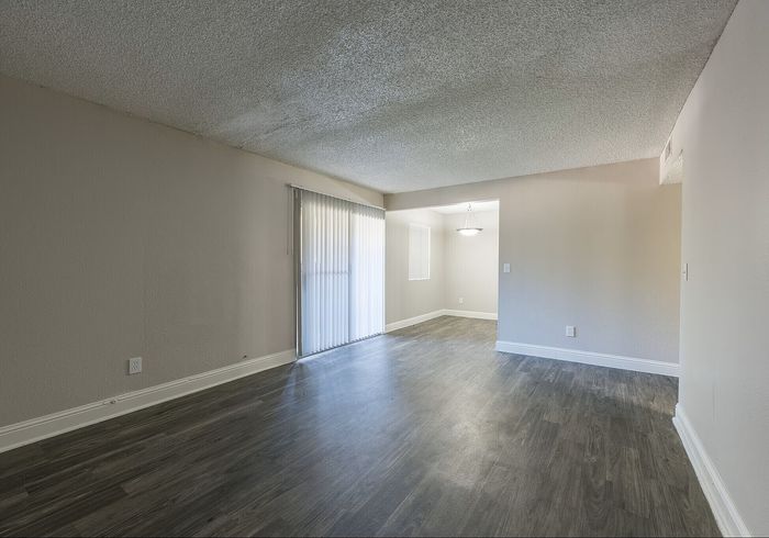 Spacious apartment with elegant wood flooring, large window with vertical blinds, and modern light fixture.