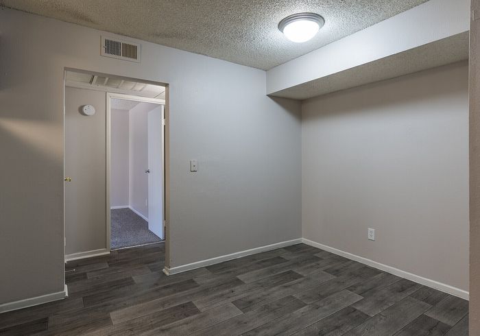 Modern apartment space with sleek gray flooring and soft ambient lighting, leading towards a cozy carpeted room.