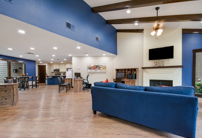 Inviting open-plan living area with a modern blue sofa, chic ceiling beams, and a cozy fireplace. Bright and spacious design ideal for relaxation or entertainment.