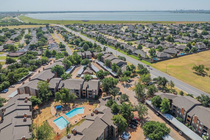 Stunning aerial view of a modern apartment complex with inviting pool, lush greenery, and panoramic lake scenery, providing a serene residential setting.