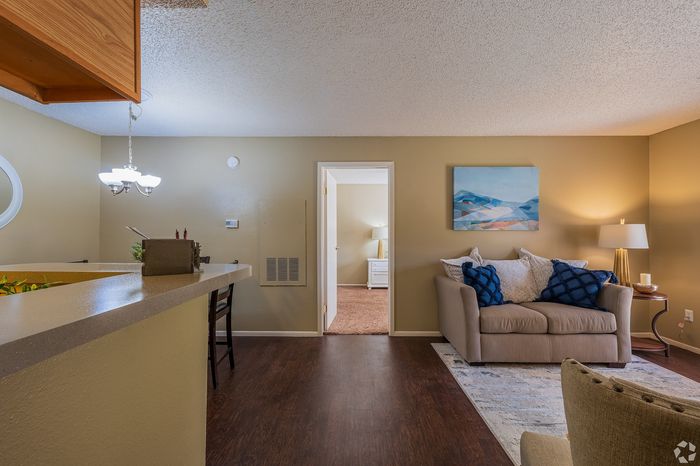 Inviting apartment living room with cozy sofa, modern artwork, and warm lighting alongside a sleek kitchen counter and dining area.