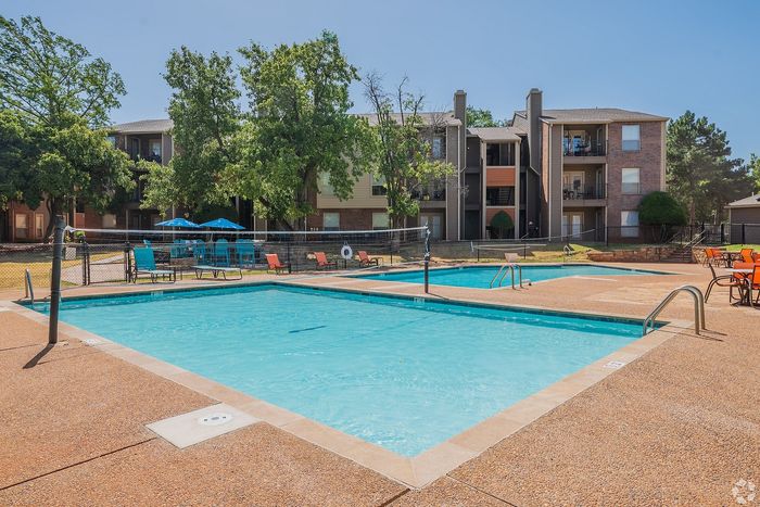 Inviting apartment complex with a sparkling outdoor swimming pool, cozy lounge chairs, and vibrant umbrellas, perfect for relaxation and enjoying sunny days.
