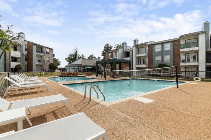 Modern apartment complex with a stunning swimming pool, sun loungers, and outdoor seating, perfect for relaxation and social gatherings.